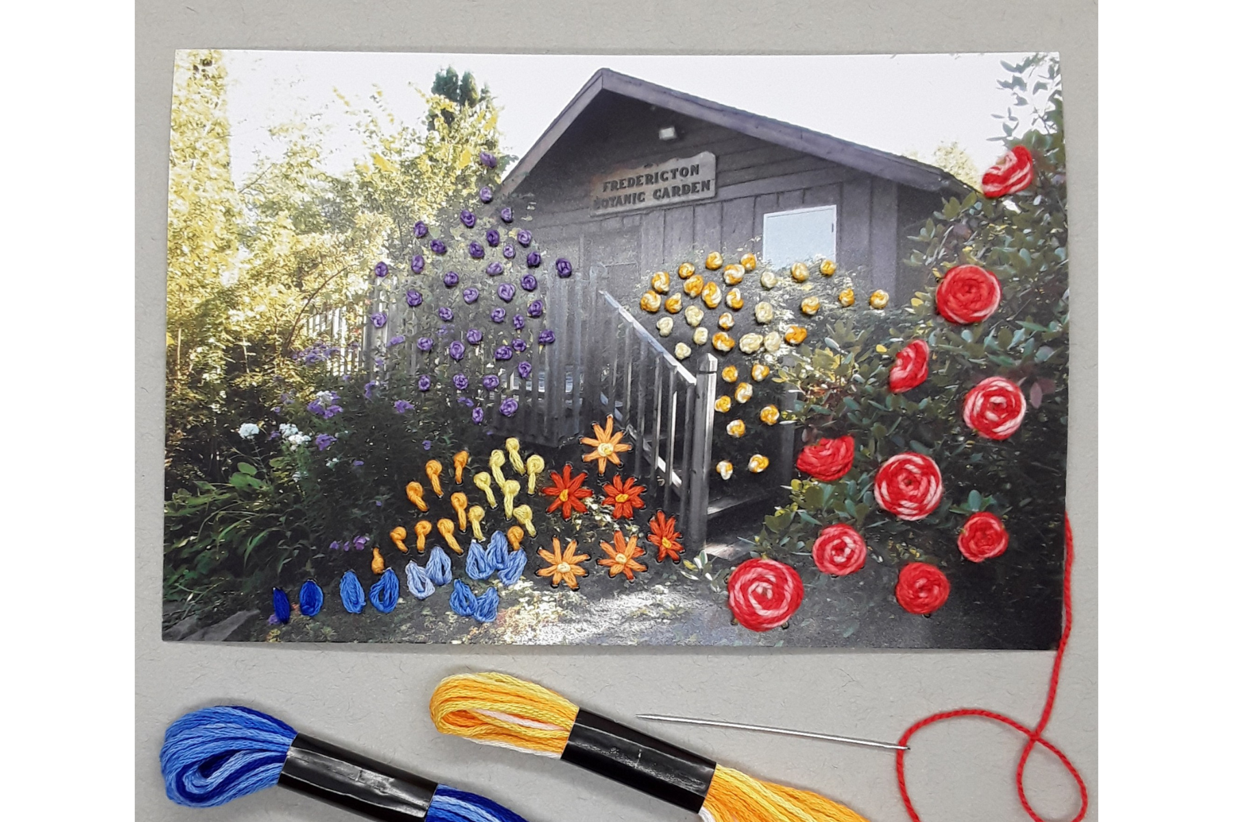 Photograph of a garden building with embroidered flowers made from blue, yellow, orange, and red threads sewn into the photograph to create a textured image.