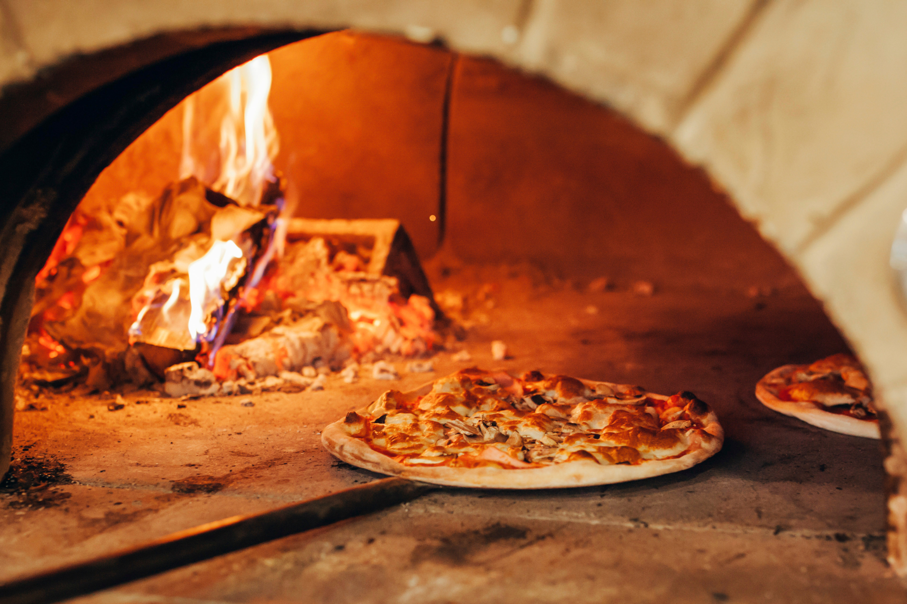 Image shows inside a wood oven of pizza cooking.