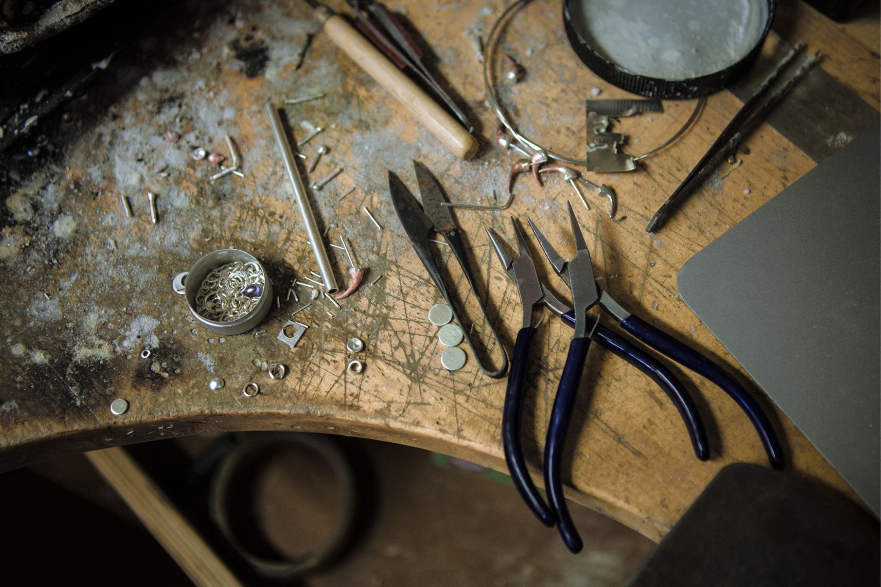 A view of a work bench. There are pieces of metal on it along with some tools for jewellery-making.