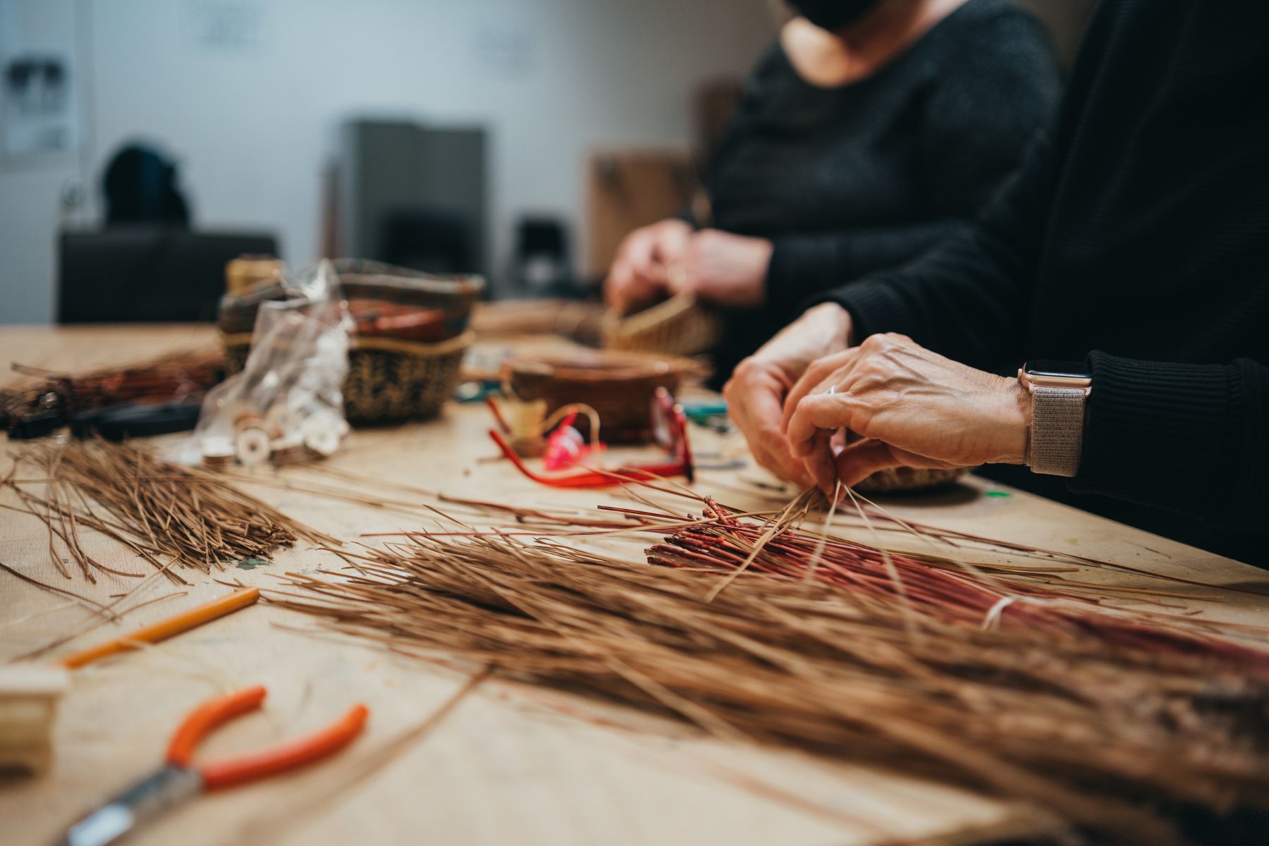 Some hands grasp and weave together some pine needles to make pine needle baskets at the Honeybee Folk School.