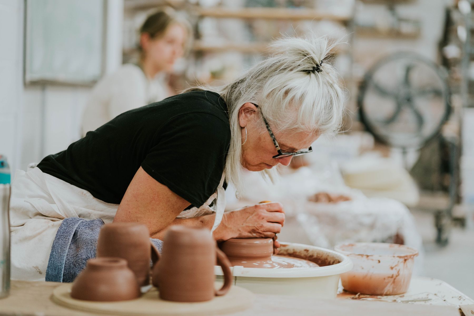 A woman leans over clay on a pottery wheel in an attempt to shape it in a workshop at the Honeybee Folk School