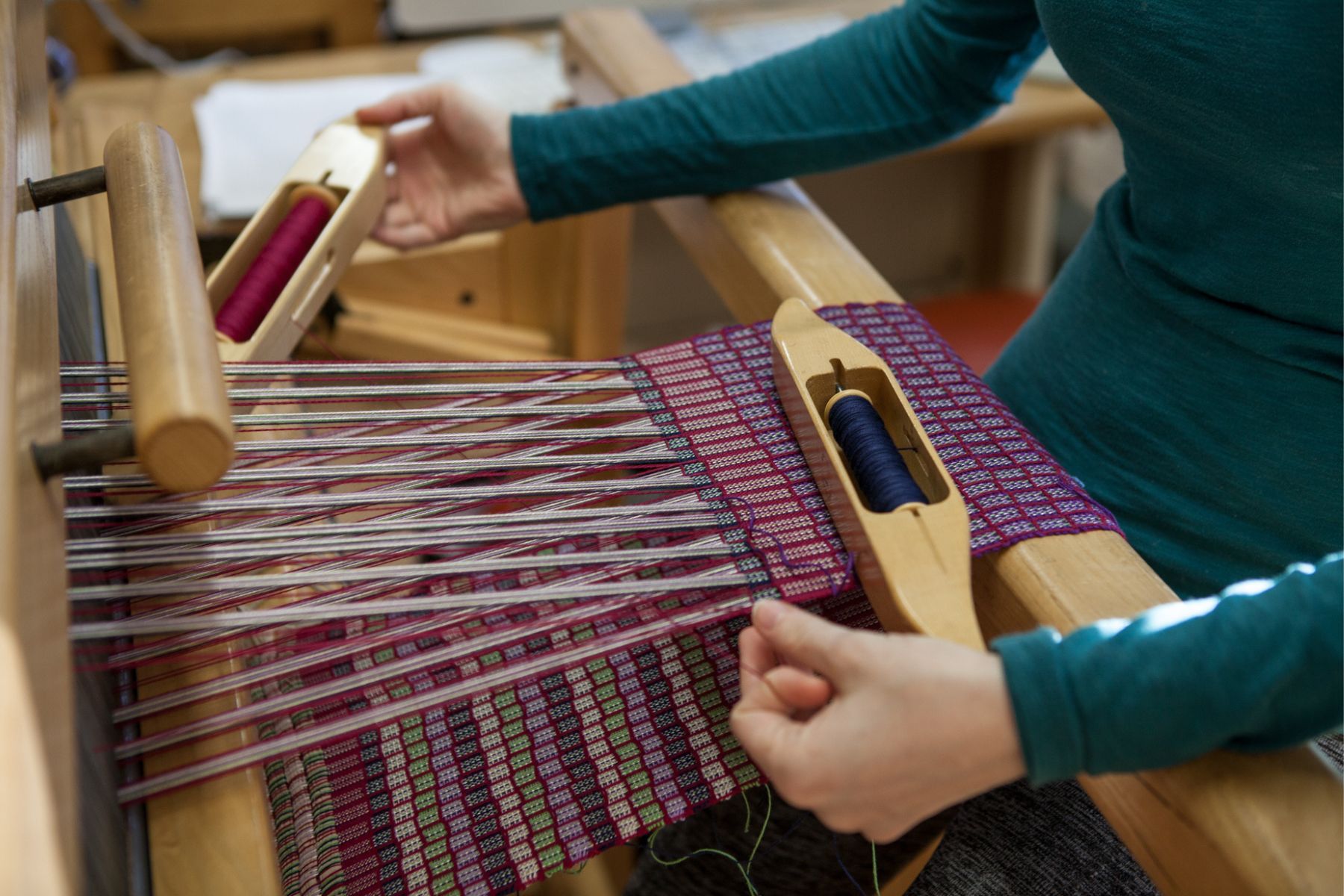 A Honeybee Folk School participant weaves purple thread on a loom at a workshop.